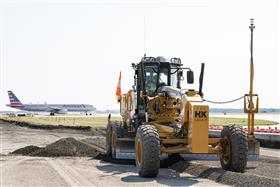 Transportation & Structures: A CAT 12M3 grades a taxiway at Philadelphia International Airport as an American Airlines jet passes by.